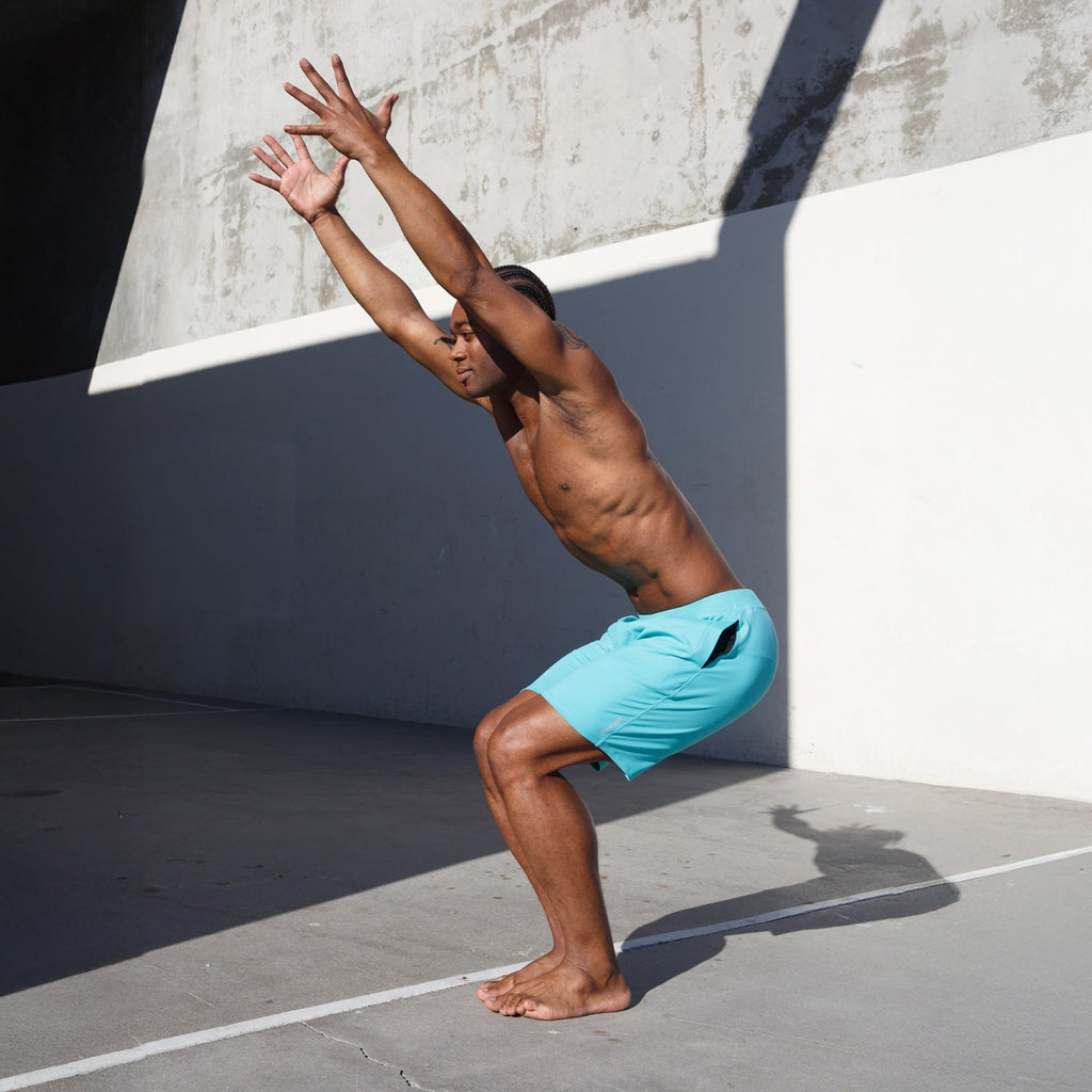 Man practicing yoga in Swerve Men's Lined Yoga Shorts 7 Inch - Aqua Blue, demonstrating a squat position.