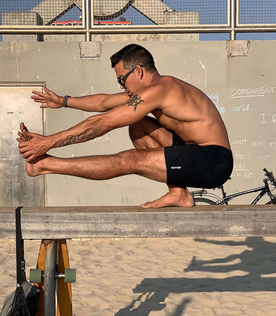 Man performing a stretch on a balance beam wearing 4-way stretch swerve shorts in Crow Black.