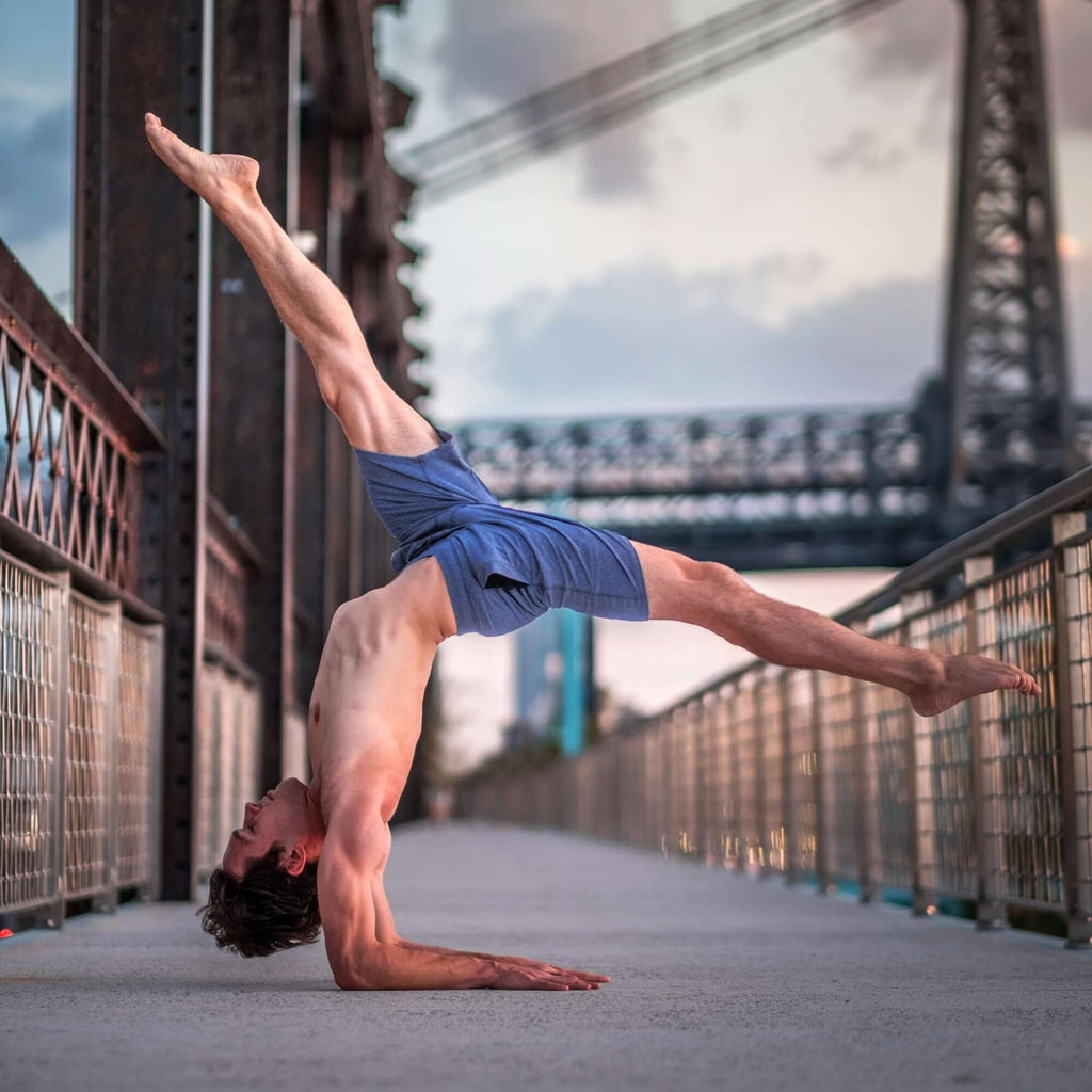 Man performing an acrobatic move in 4-way stretch Swerve Shorts, showcasing flexibility and movement support.